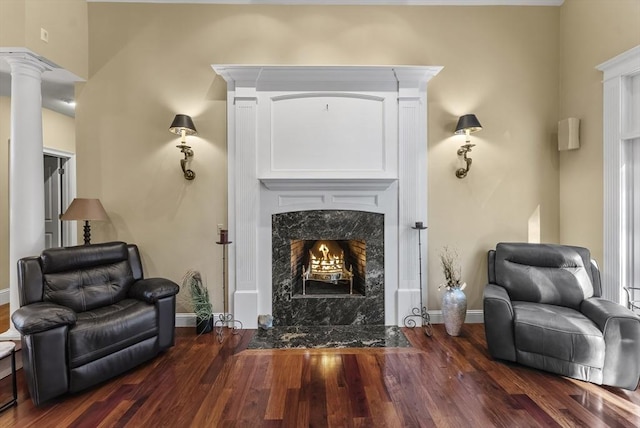 living area with dark wood-type flooring, ornate columns, and a fireplace