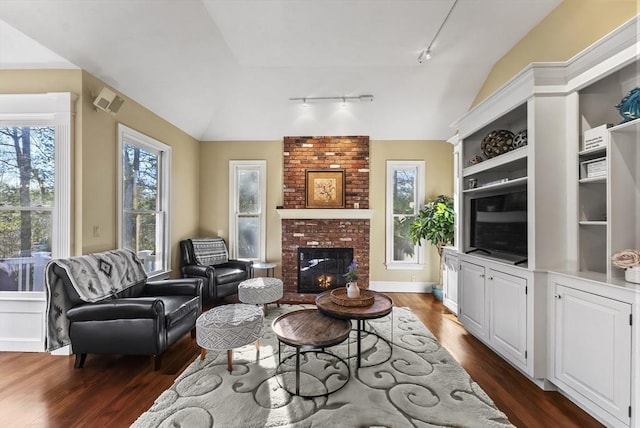 living room with vaulted ceiling, a brick fireplace, dark hardwood / wood-style flooring, and track lighting