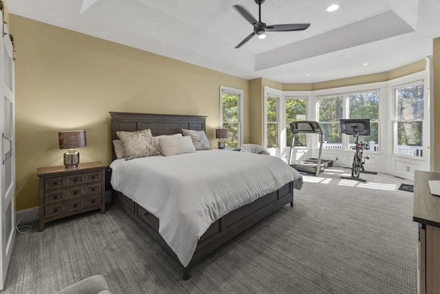 bedroom featuring ceiling fan, a raised ceiling, dark colored carpet, and multiple windows