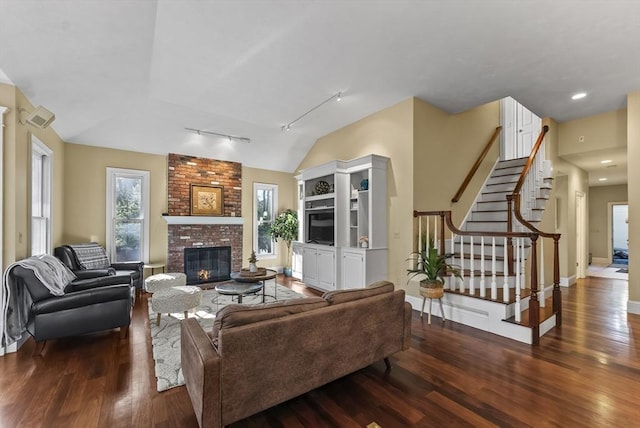 living room with a brick fireplace, rail lighting, vaulted ceiling, and dark wood-type flooring