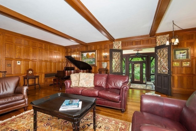 living room featuring wood walls, beamed ceiling, hardwood / wood-style flooring, and ceiling fan with notable chandelier