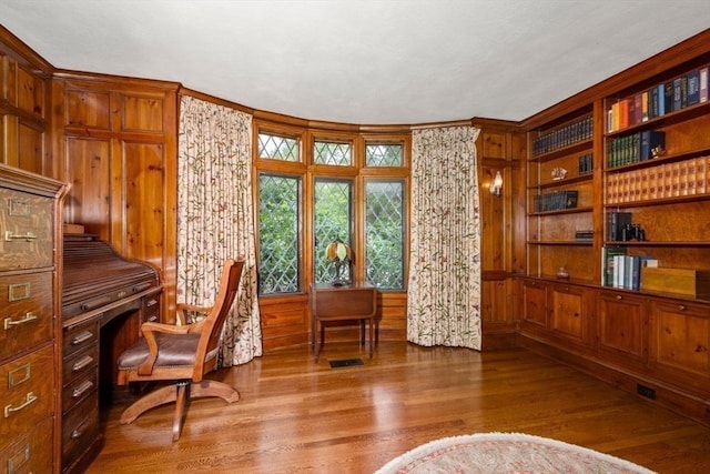 home office featuring built in desk, ornamental molding, wooden walls, and dark hardwood / wood-style flooring