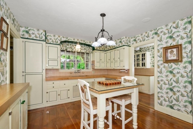 kitchen with dark hardwood / wood-style floors, pendant lighting, a notable chandelier, sink, and butcher block counters