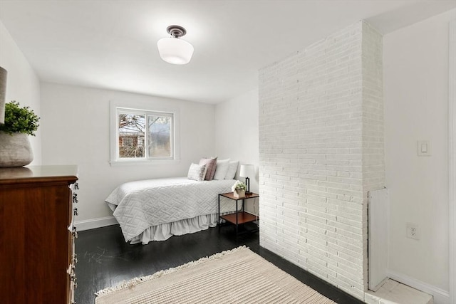 bedroom featuring brick wall and dark hardwood / wood-style flooring