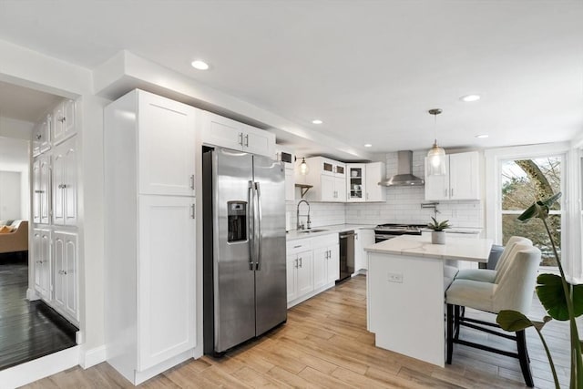 kitchen with a kitchen island, appliances with stainless steel finishes, decorative light fixtures, white cabinets, and wall chimney range hood