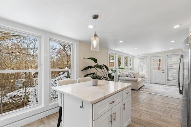 kitchen with decorative light fixtures, white cabinetry, stainless steel fridge, a kitchen breakfast bar, and light stone countertops