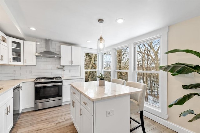 kitchen featuring white cabinetry, stainless steel appliances, light stone counters, and wall chimney range hood