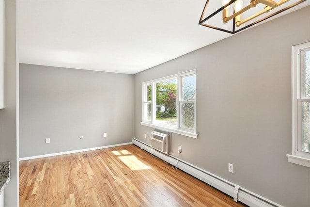 spare room featuring an inviting chandelier, an AC wall unit, baseboards, light wood-type flooring, and a baseboard radiator