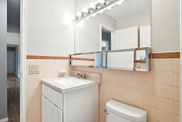 bathroom with tile walls, a wainscoted wall, vanity, and toilet