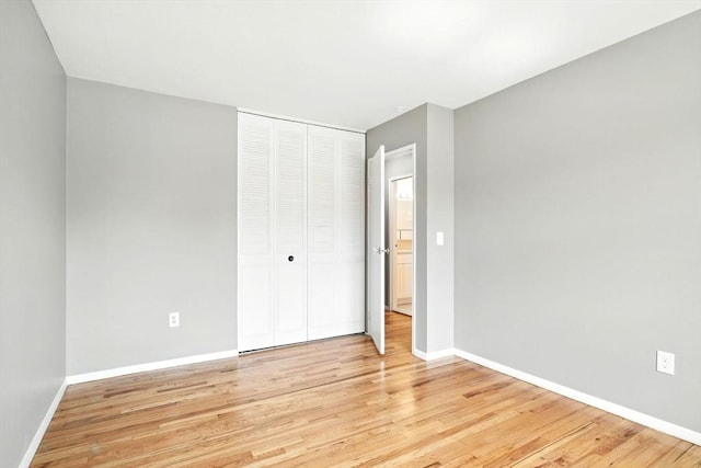 unfurnished bedroom featuring baseboards, light wood-style flooring, and a closet