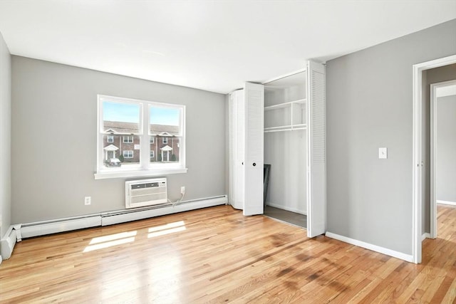 unfurnished bedroom featuring wood finished floors, baseboards, a baseboard radiator, a closet, and an AC wall unit