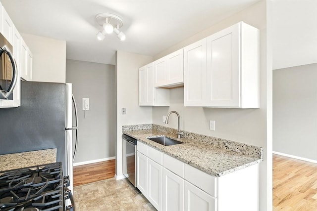 kitchen featuring white cabinets, light stone countertops, appliances with stainless steel finishes, a sink, and baseboards