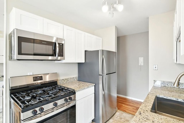 kitchen with a sink, white cabinetry, light stone countertops, and stainless steel appliances
