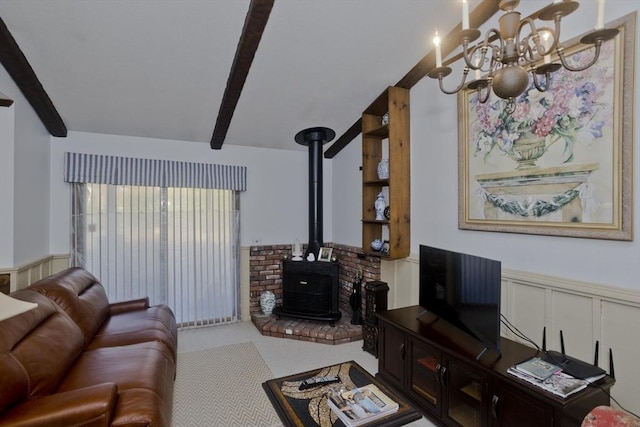 living room with carpet flooring, wainscoting, a wood stove, a notable chandelier, and a decorative wall