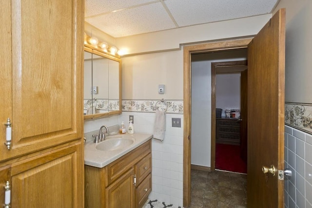 bathroom featuring a wainscoted wall, a paneled ceiling, tile walls, and vanity