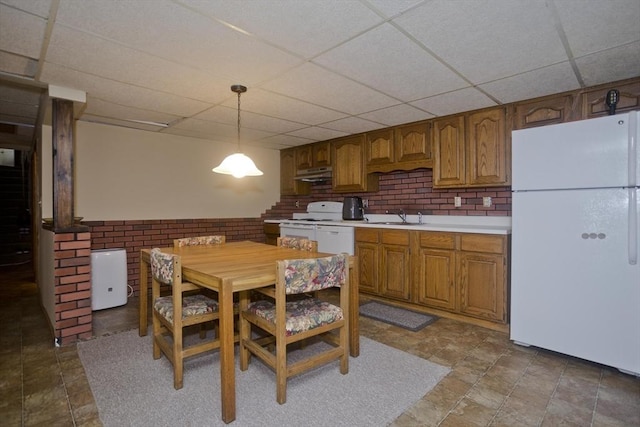 kitchen featuring under cabinet range hood, light countertops, brown cabinetry, white appliances, and a sink