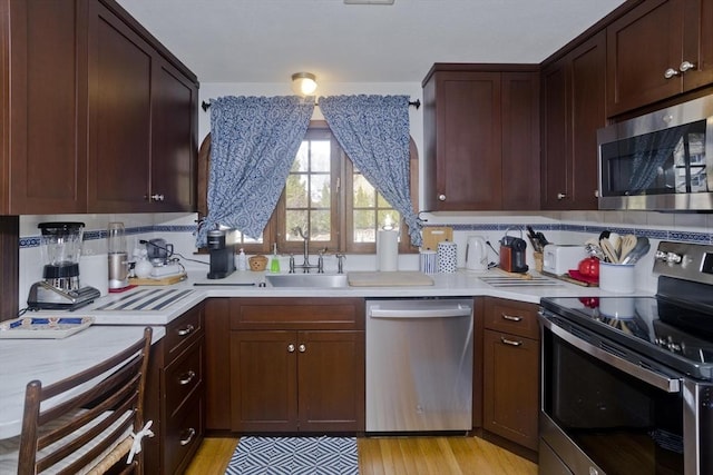 kitchen with light wood-type flooring, stainless steel appliances, light countertops, and a sink