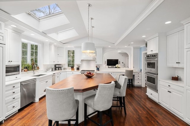 kitchen featuring vaulted ceiling with skylight, a breakfast bar area, appliances with stainless steel finishes, a center island, and a sink