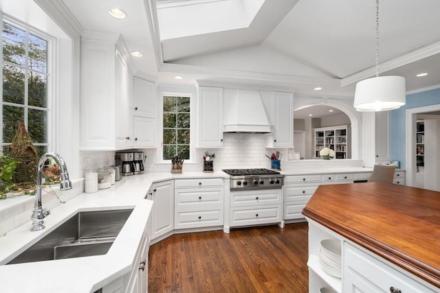 kitchen with dark wood-style floors, stainless steel gas cooktop, custom range hood, a sink, and vaulted ceiling