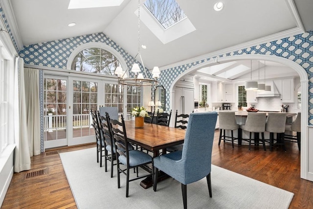 dining space with arched walkways, lofted ceiling with skylight, visible vents, and wallpapered walls