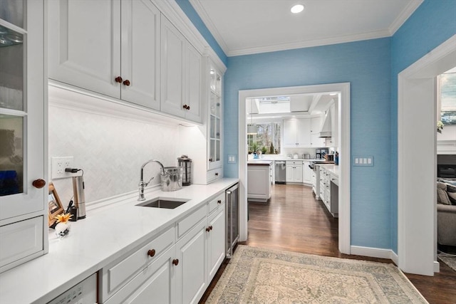 kitchen with dark wood-style flooring, a sink, white cabinets, stainless steel dishwasher, and crown molding