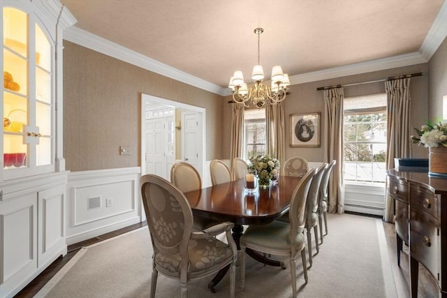 dining space featuring wainscoting, an inviting chandelier, crown molding, a baseboard heating unit, and a decorative wall