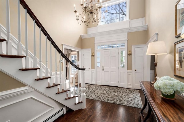 foyer entrance with wainscoting, wood finished floors, a high ceiling, baseboard heating, and a notable chandelier