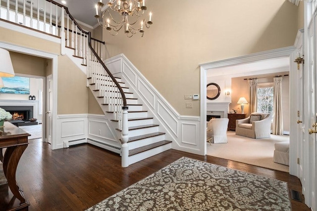 stairs with crown molding, a lit fireplace, a towering ceiling, and wood finished floors