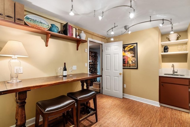 bar with baseboards, indoor wet bar, a sink, and light wood-style floors