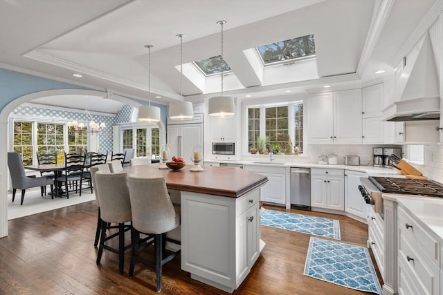 kitchen featuring a center island, white cabinets, custom exhaust hood, decorative backsplash, and crown molding