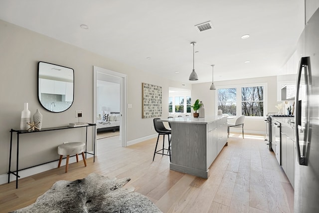 kitchen with a large island, stainless steel fridge, hanging light fixtures, light wood-type flooring, and gray cabinetry