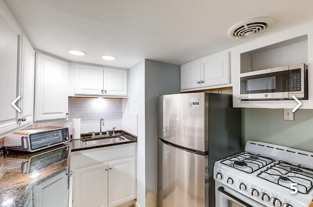 kitchen featuring white cabinetry, stainless steel appliances, dark stone countertops, sink, and backsplash