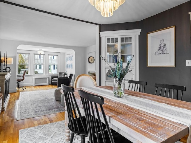 dining space featuring baseboards, light wood finished floors, an inviting chandelier, radiator heating unit, and arched walkways