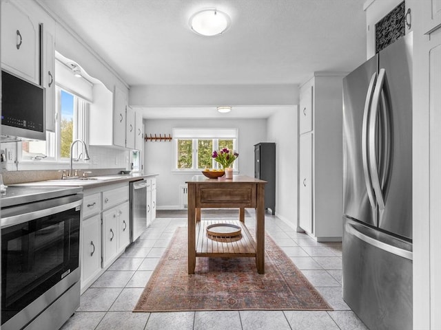 kitchen featuring backsplash, stainless steel appliances, light tile patterned flooring, white cabinetry, and a sink