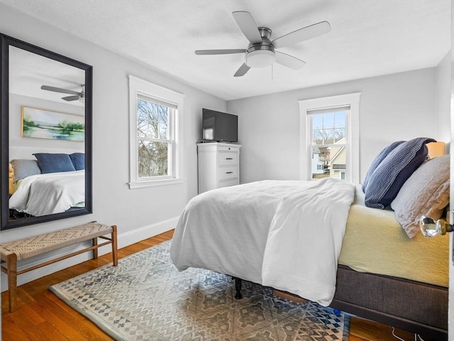 bedroom with ceiling fan, baseboards, multiple windows, and wood finished floors