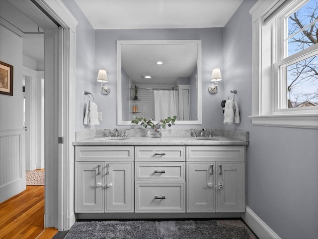 bathroom featuring a shower with shower curtain, double vanity, wood finished floors, and a sink