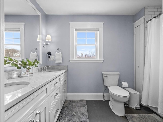 full bath featuring baseboards, double vanity, a sink, tile patterned flooring, and toilet