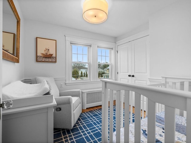 bedroom featuring a closet, radiator heating unit, a nursery area, and dark wood-style flooring