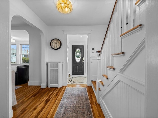 entryway featuring baseboards, arched walkways, wood finished floors, and stairs