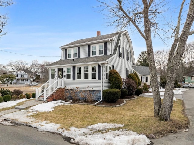 colonial inspired home with a gambrel roof, a chimney, a front lawn, and a shingled roof