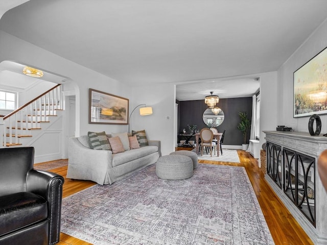 living area with arched walkways, a notable chandelier, stairs, and wood finished floors