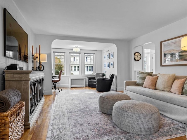 living area featuring baseboards, arched walkways, wood finished floors, and radiator heating unit