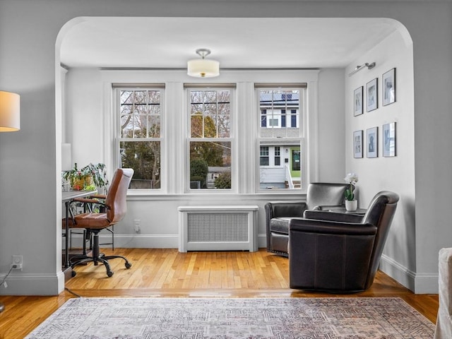 living area featuring arched walkways, radiator, and wood finished floors