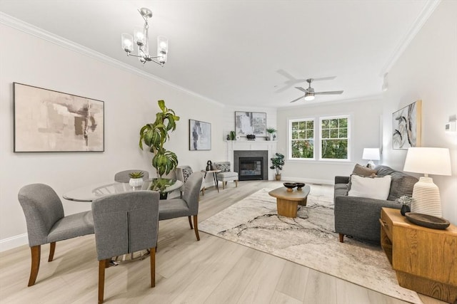 living room with light wood-style floors, a glass covered fireplace, crown molding, and ceiling fan with notable chandelier