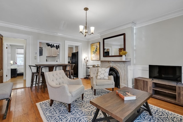 living room with light wood-type flooring, crown molding, a premium fireplace, and a notable chandelier