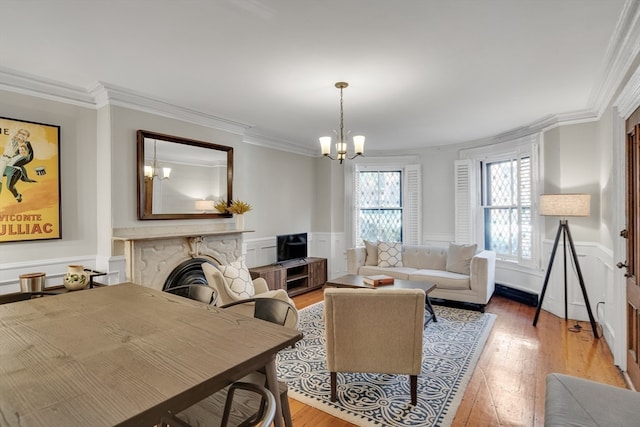 living room featuring ornamental molding, hardwood / wood-style flooring, an inviting chandelier, and a stone fireplace