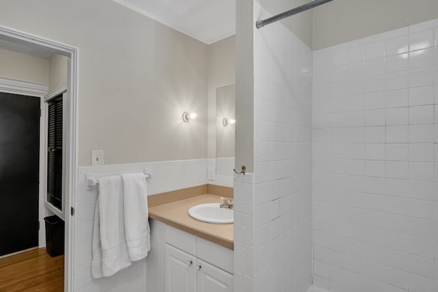 bathroom featuring vanity, hardwood / wood-style floors, tiled shower, tile walls, and ornamental molding