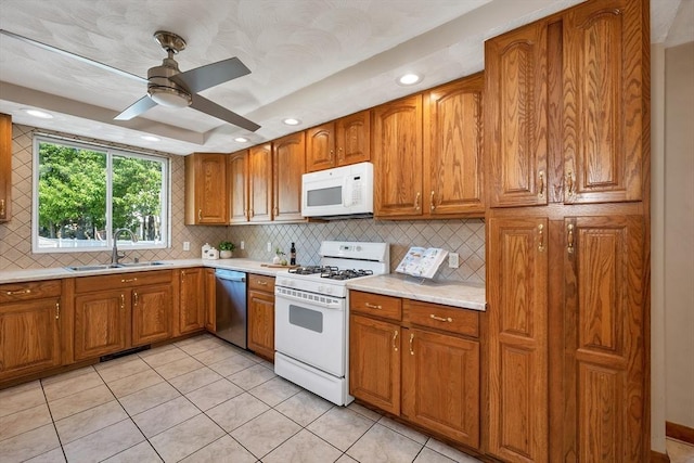 kitchen featuring white appliances, a sink, brown cabinetry, light countertops, and recessed lighting