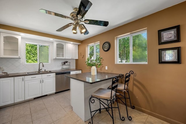 kitchen with dishwasher, a kitchen bar, glass insert cabinets, a sink, and white cabinets