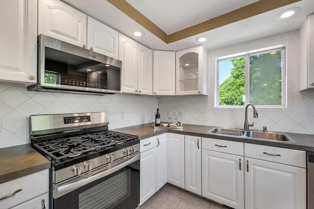kitchen featuring stainless steel appliances, a sink, dark countertops, white cabinets, and recessed lighting
